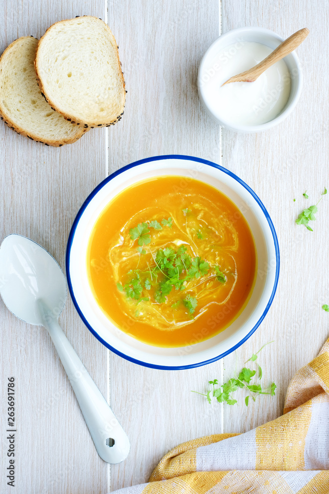Pumpkin soup in white bowl with cream and parsley. Light wooden background