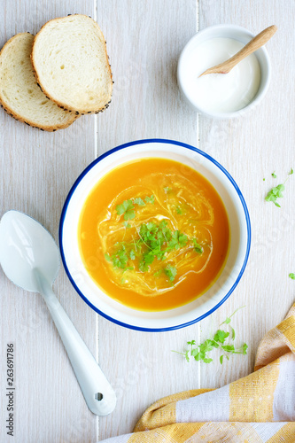 Pumpkin soup in white bowl with cream and parsley. Light wooden background