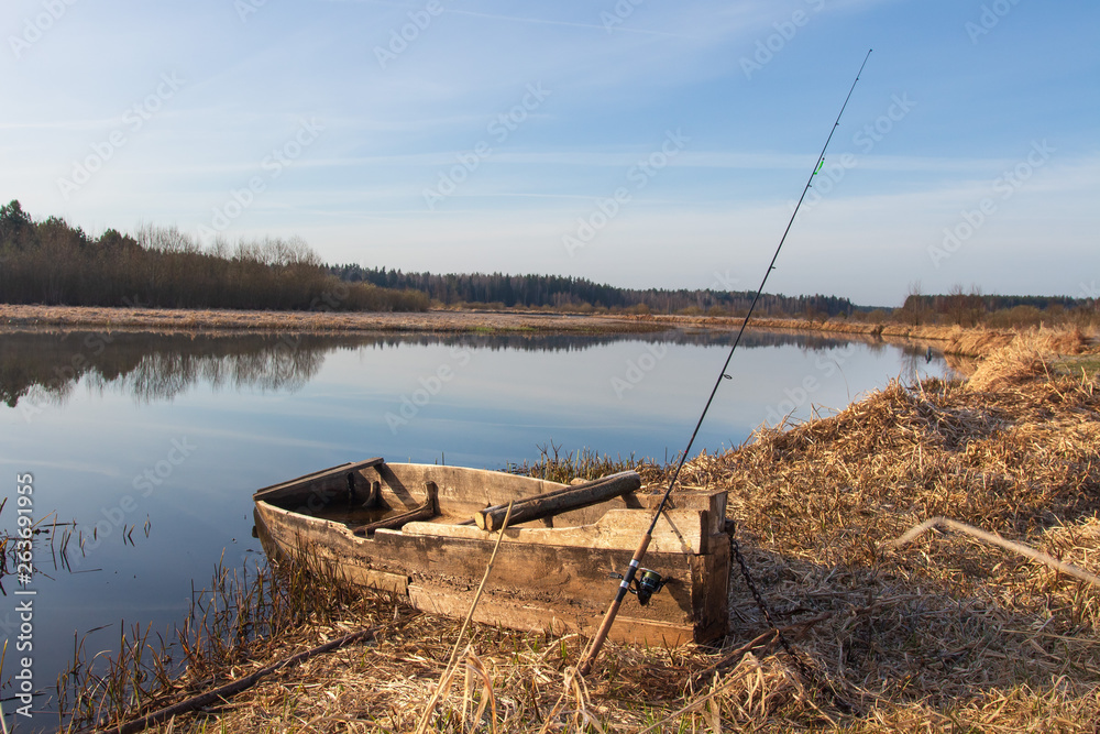 Rural landscape with boat and fishing rod on river side at spring. Fishing