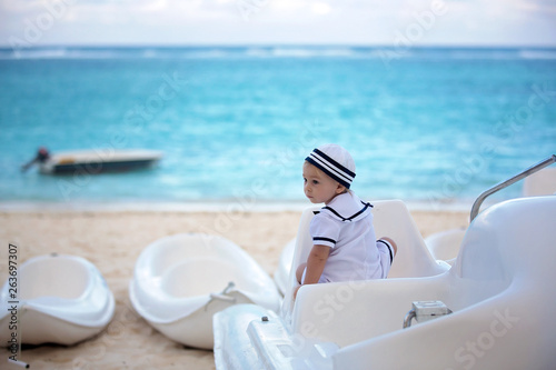 Beautiful toddler boy, dressed as a sailor, playing on the beach on sunset, enjoying tropical magical holiday vacation © Tomsickova