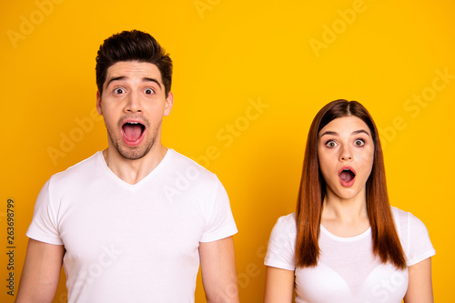 Close up photo two cool amazing beautiful she her he him his couple standing side by side open mouth eyes unbelievable success wear casual white t-shirts outfit clothes isolated yellow background