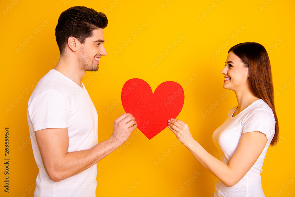 Close up side profile photo amazing beautiful she her he him his guy lady look eyes lovely hold hands arms big paper heart figure postcard wear casual white t-shirts isolated yellow background Close up side profile photo amazing beautiful she her he him his guy lady look eyes lovely hold hands arms big paper heart figure postcard wear casual white t-shirts isolated yellow background