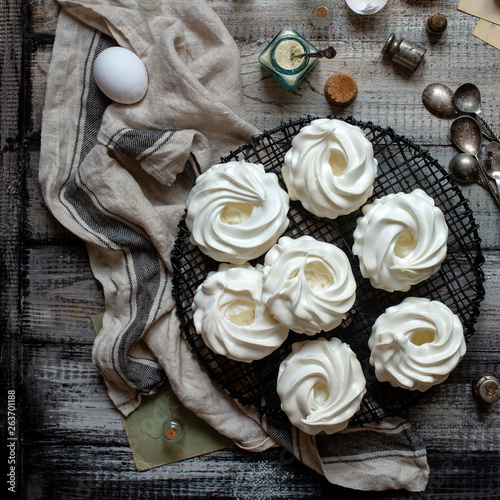 Overhead shot of homemade white mini meringue desserts pavlova on wicker metal stand on grey wooden table