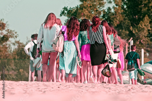 tourists from the back walk along the beach barefoot in the sunshine in pink,