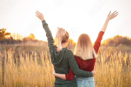 Two young women standing on the field and rise up hands at sunset.