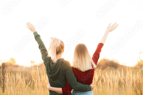 Two young female standing on the field and rise up hands. Best friends