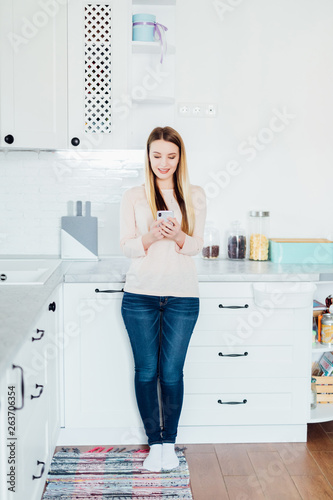 Young beautiful woman using cell phone in the kitchen