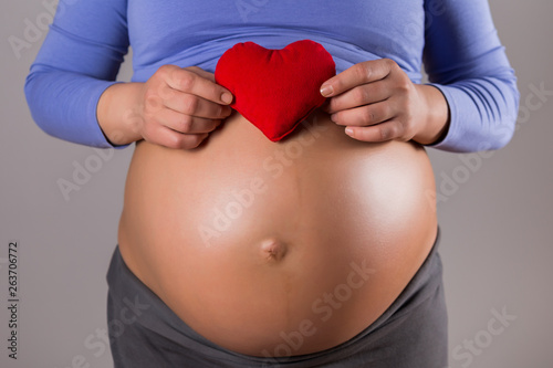 Wallpaper Mural Image of close up stomach of pregnant woman holding red heart  on gray background. Torontodigital.ca