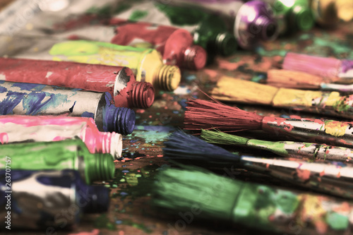 Stained paint brushes and acrylic pain tubes on artist table. Artistic background