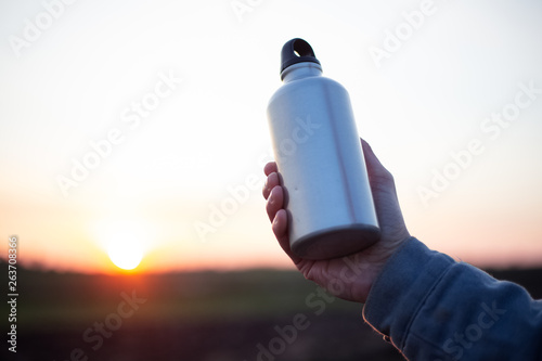 Hand of man holding aluminium bottle for water, on background of sunset.