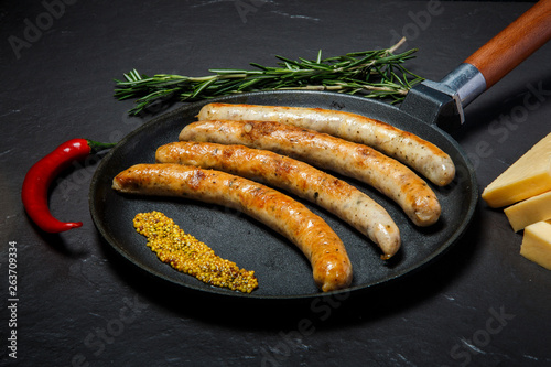 big frying pan with grilled thin sausages and mustard