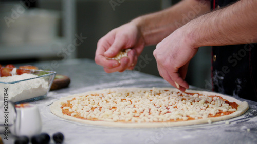 Restaurant kitchen. A chef putting cheese on the pizza