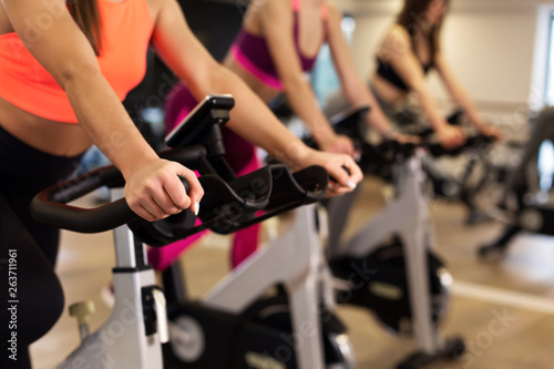 Group of young slim women workout on exercise bike in gym. Sport and wellness lifestyle concept