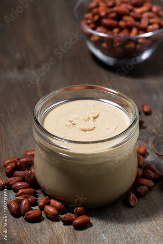 peanut butter in a glass jar on a wooden background, vertical