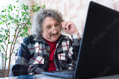 A pensioner in glasses working at the computer at home. Ageing, lifestyle.
