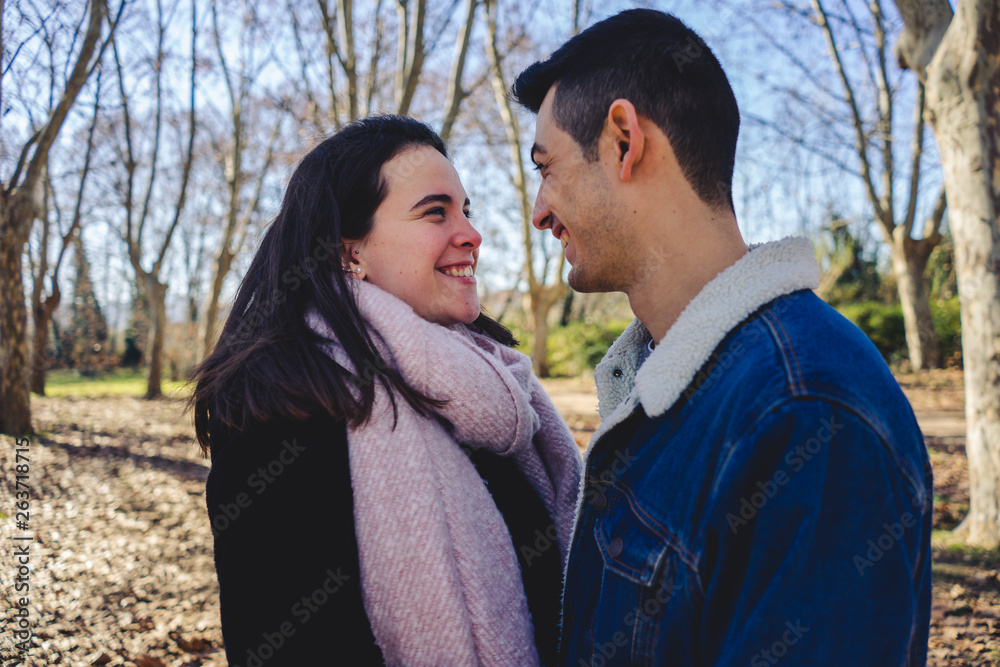 Naklejka premium Happy young couple smiling together in a sunny forest on an autumn day.