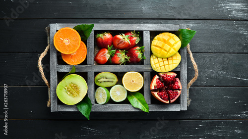 Fototapeta Naklejka Na Ścianę i Meble -  Fruits in a wooden box. Citrus, melon, pomegranate, strawberry, banana. Top view. Free space for your text.