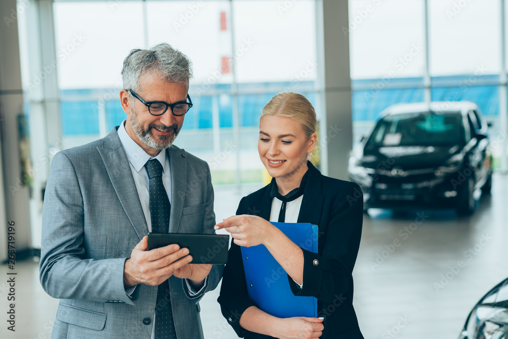 salesman showing woman online car gadgets in car dealership showroom salesman showing woman online car gadgets in car dealership showroom