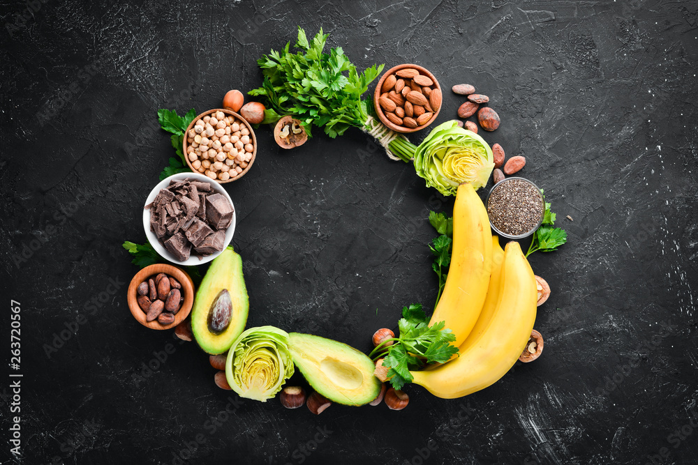 Foods containing natural magnesium. Mg: Chocolate, banana, cocoa, nuts, avocados, broccoli, almonds. Top view. On a black background.