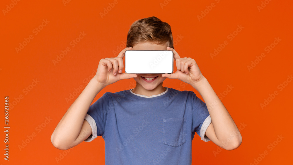 Happy modern teen boy covering eyes with blank smartphone