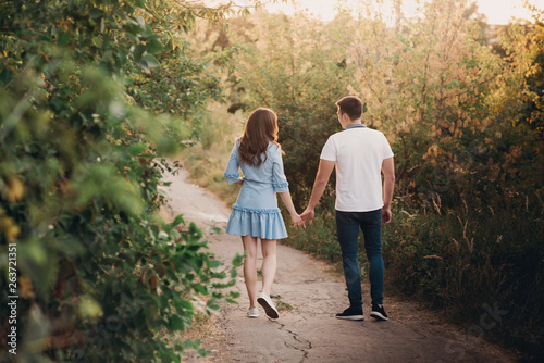 Back view couple walking away in the field, view of couple holding hands, lovers walking holding hands