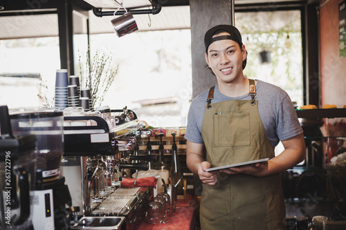 asian man barista holding tablet for checking order from customer on coffee cafe.