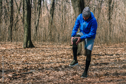 A man in training clothes got a knee injury while jogging in outdoor workout. Concept of sports injury, running technique, wrong running, tendonitis, a large load.