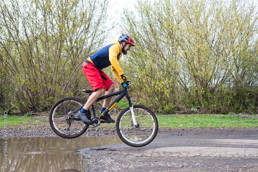 A cyclist in red shorts and a yellow jacket riding a bicycle along a street with puddles. A cyclist in red shorts and a yellow jacket riding a bicycle along a street with puddles.