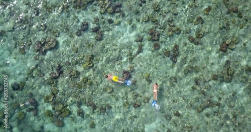 A young man and woman snorkel through a tropical reef in the Philippines, surrounded by clear, shallow water as the camera turns to follow them. Lookdown aerial, follow, 4k. photo