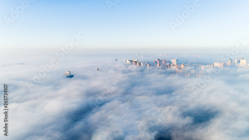 The city is covered with thick fog and protruding from it where neither where high-rise buildings