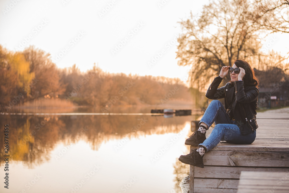young pretty fashion woman sitting on pier on sunset with beautiful view of river young pretty fashion woman sitting on pier on sunset with beautiful view of river
