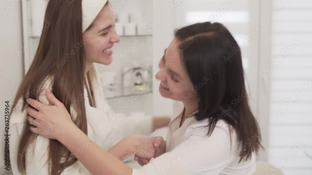 Attractive young woman after an appointment with her female cosmetologist is saying goodbye. Both women are holding their hands to farewell and smiling. Attractive young woman after an appointment with her female cosmetologist is saying goodbye. Both women are holding their hands to farewell and smiling.