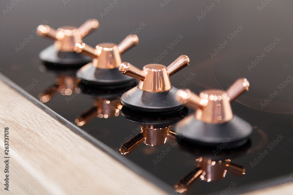 Obraz premium Closeup of the copper knob switch plates are reflected in the black shiny electric or gas hob for the kitchen. Concept modern household appliances in vintage style