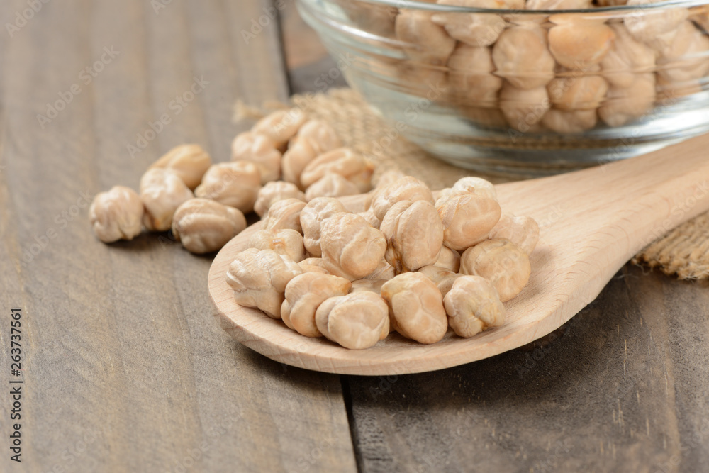 Garbanzos gordos en un cuenco de cristal y una cuchara de madera sobre fondo de madera Garbanzos gordos en un cuenco de cristal y una cuchara de madera sobre fondo de madera