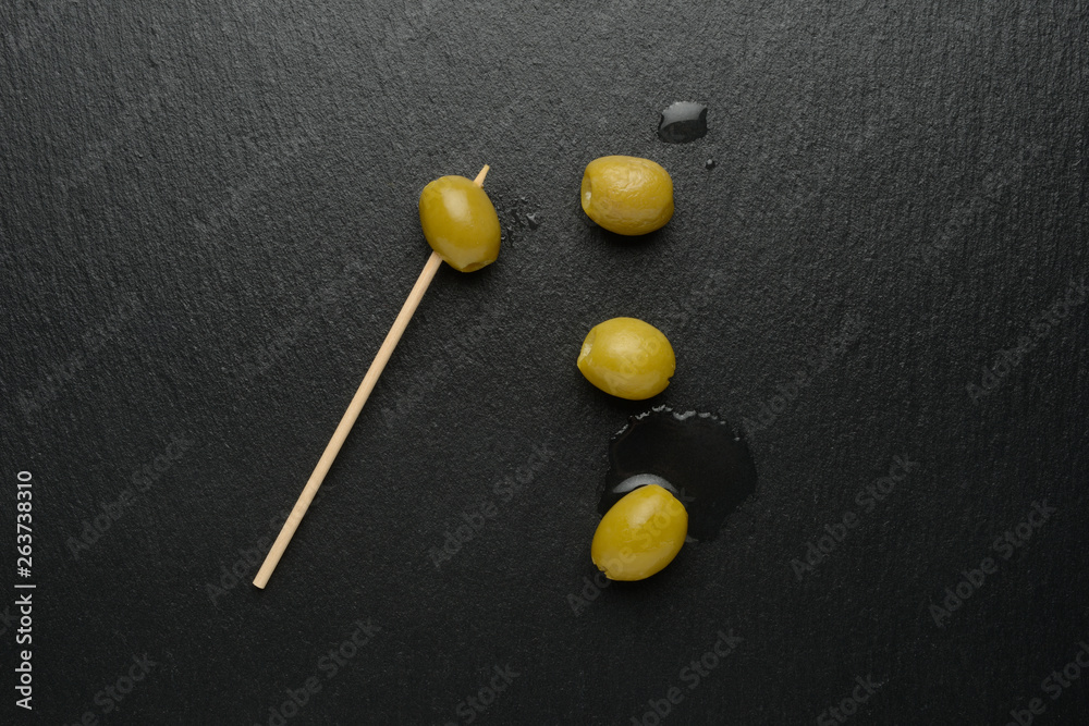 Aceitunas verdes y palillos en la tabla de piedra negra