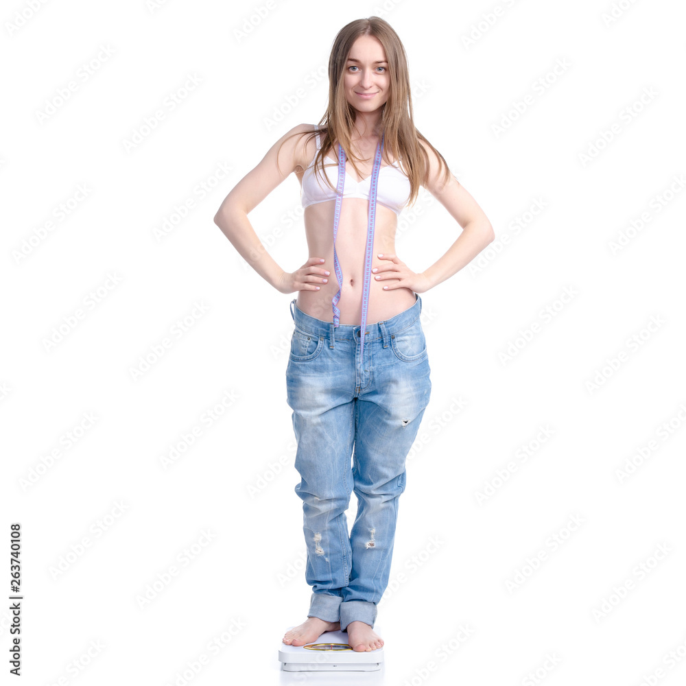 Obraz premium Beautiful woman in big jeans on weighing-machine with centimeter in hand, weight loss slimming on a white background. Isolation