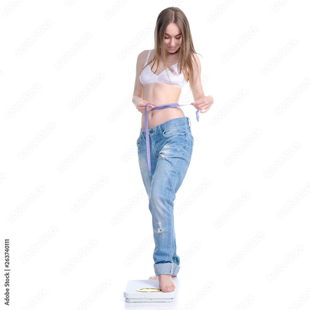 Beautiful woman in big jeans on weighing-machine with centimeter in hand, weight loss slimming on a white background. Isolation Beautiful woman in big jeans on weighing-machine with centimeter in hand, weight loss slimming on a white background. Isolation