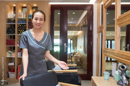 Smiling hair stylist welcoming guest to sit down