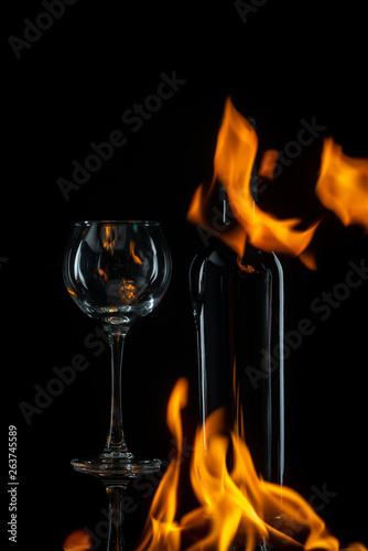 transparent wineglass with bottle and spurts of flame on black background 
