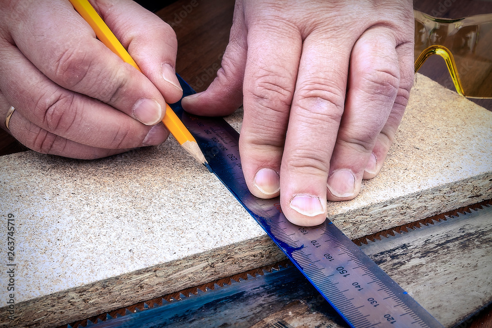 A person marks a wooden board with a pencil and ruler A person marks a wooden board with a pencil and ruler