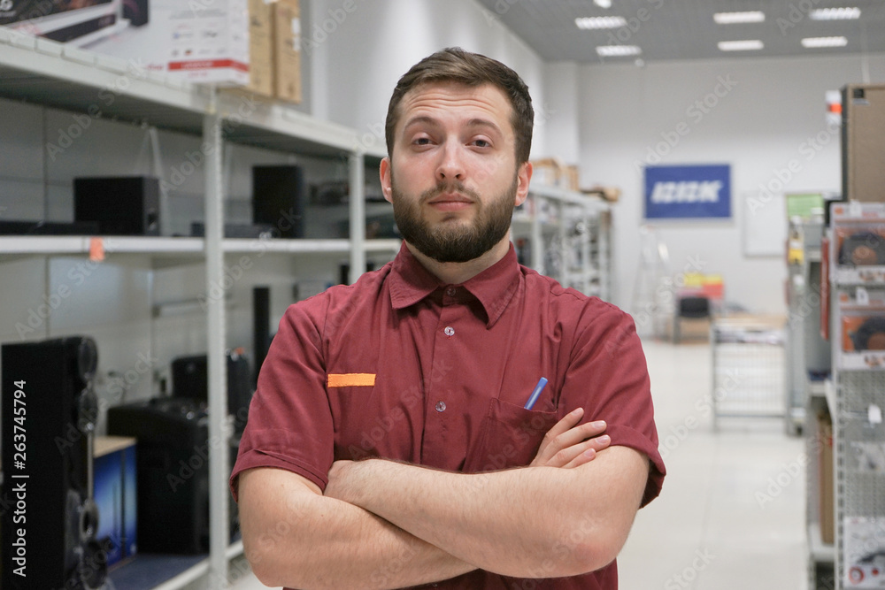 Fototapeta premium Portrait of a Professional Expert Consultant Smiles and Looks into Camera as Stands in the Bright, Modern Electronics Store Full of Latest Models of TV Sets, Cameras, Tablets and other Devices. 