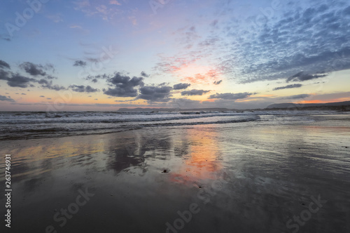 Enchanting sunset. Storm sea with high waves. Unbelievable blue, pink, orange colors of the sky are reflected on the wet sand. The mountains in haze on the horizon. Crete island, Greece.