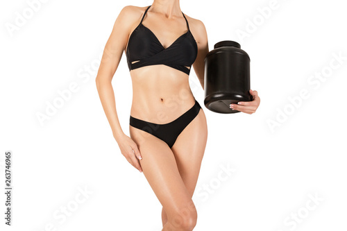 Female sexy taned fit cropped body in black top and panties with big plastic jar of sport nutrition, isolated on white