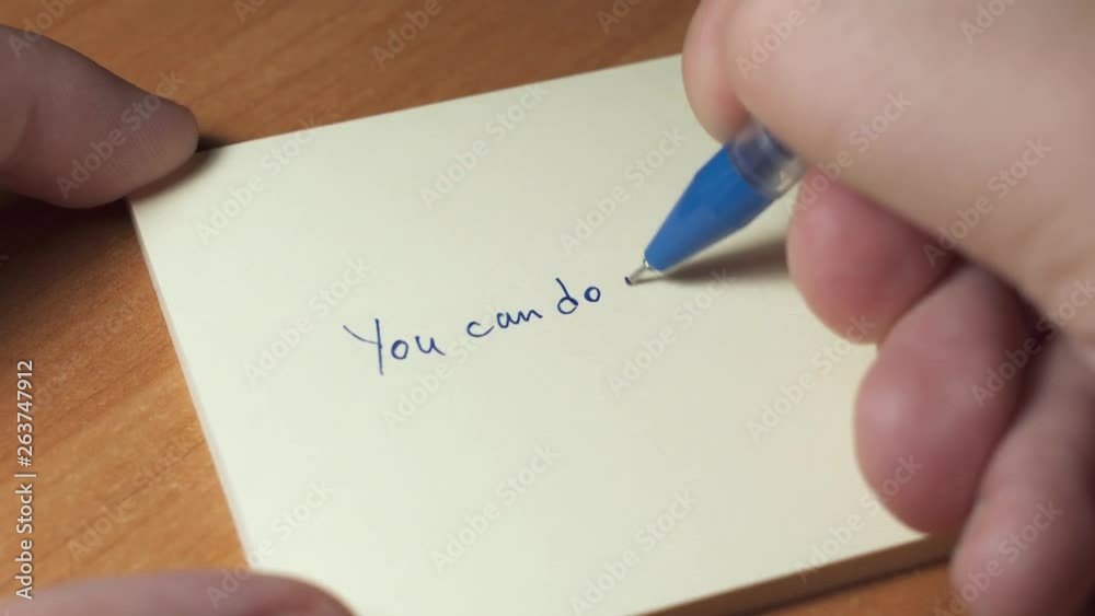 Motivation, inspiration, personal growth concept. Someone is writing inspiring phrase on a sticker paper Motivation, inspiration, personal growth concept. Someone is writing inspiring phrase on a sticker paper