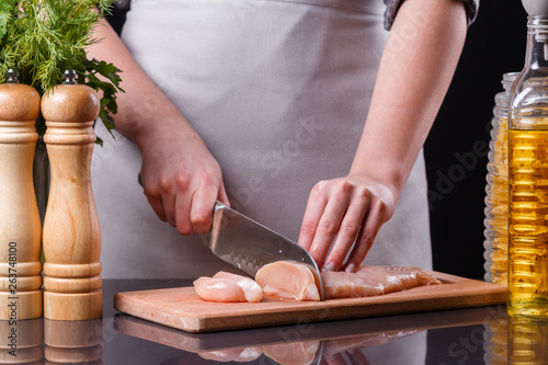 young woman in a gray apron cuts chicken breast