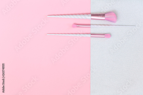 Three unicorn makeup brushes on silver pink background. Flat lay with copy space, beauty and cosmetics blogger concept