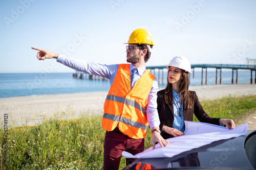 Ingegneri discutono su un progetto di un pontile marino sulla spiaggia vicino al mare. Indicano dove avverrà la futura costruzione. photo
