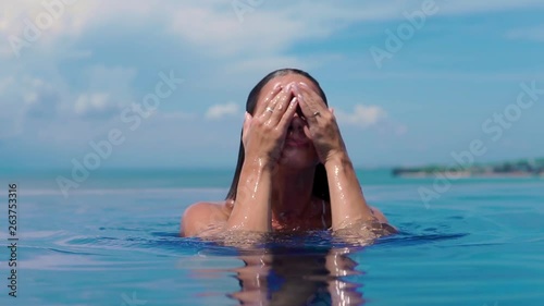 The beautiful girl comes up from pool and from it water flows down. Close up. Female Enjoying Summer Travel In Swimming Pool At Luxury Resort