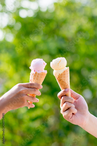 woman holding and eating ice cream in the park. Hands holding melting ice cream waffle cone in hand on summer nature light background. Two colorful tasty ice cream cones in hand.