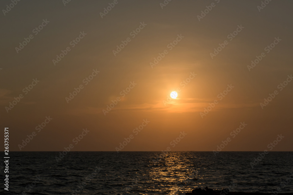 Bright sunset with large yellow sun under the sea surface. sunrise in the sea. Beautiful sunset above the sea. Tropical sunset on the beach.